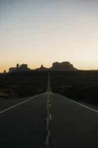 Empty desert highway leading toward red rock buttes at sunset
