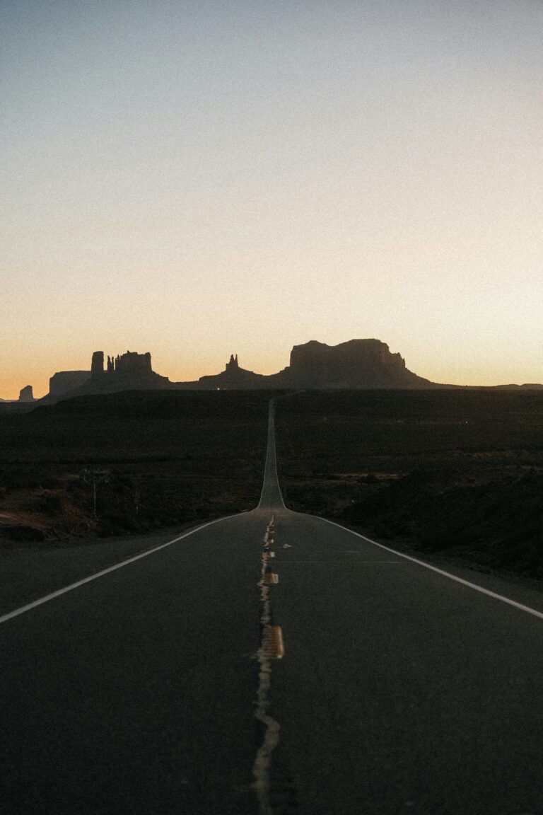 Empty desert highway leading toward red rock buttes at sunset