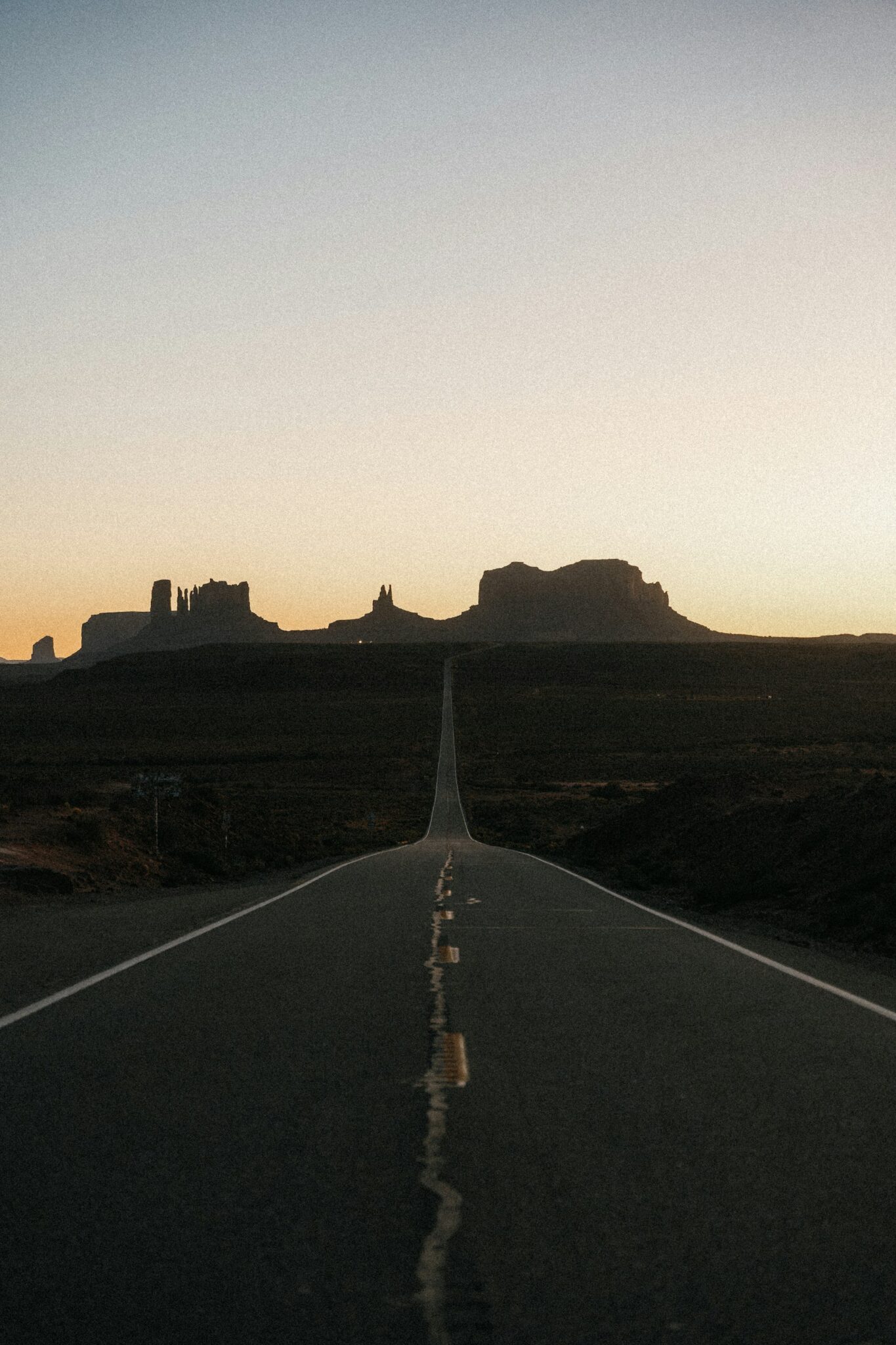 Empty desert highway leading toward red rock buttes at sunset